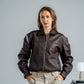 Woman wearing a brown leather jacket and beige pants against a plain background