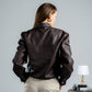 Person wearing a dark leather jacket and beige pants against a plain background