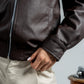 Person wearing a brown leather jacket with a neutral background