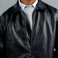 Man wearing a black leather jacket over a gray sweater on a gray background
