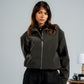 Woman wearing a dark green jacket and black pants against a plain background
