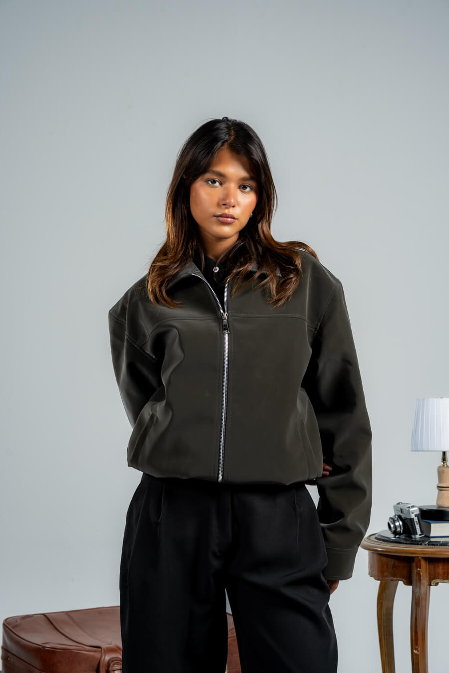 Woman wearing a dark green jacket and black pants against a plain background