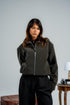 Woman wearing a dark green jacket and black pants against a plain background