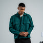 Man wearing a green jacket and black pants against a plain background