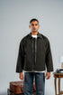 Man wearing a dark jacket over a white shirt with a gray background