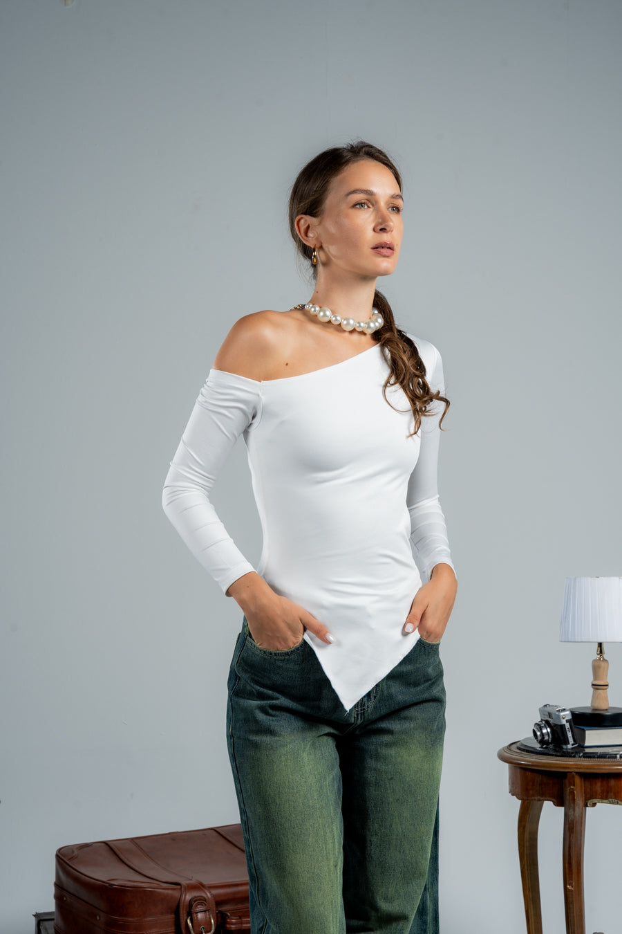 Woman wearing a white long-sleeve top and green pants against a plain background