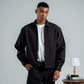 Man wearing a black jacket and pants standing in a room with a table and lamp.