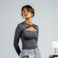 Woman wearing a gray long-sleeve top with cut-out design and light gray pants against a plain background.