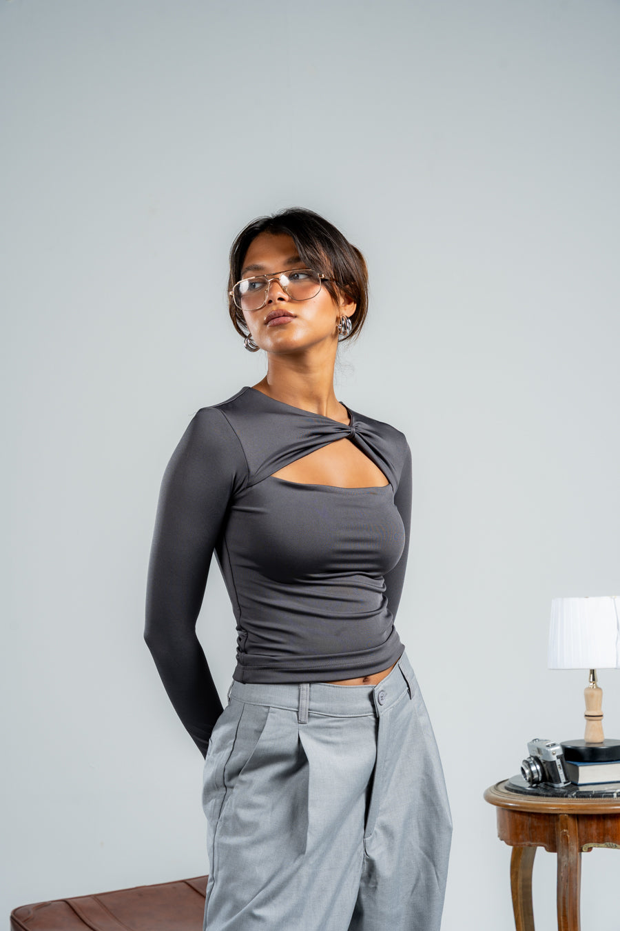 Woman wearing a gray long-sleeve top with cut-out design and light gray pants against a plain background.