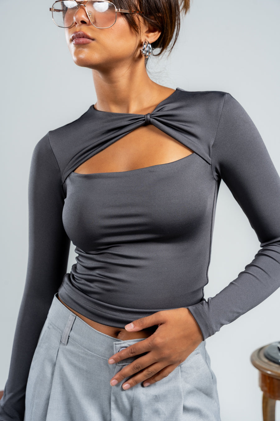 Woman wearing a gray long-sleeve top with a knot detail on a plain background