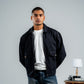 Man wearing a black jacket over a white shirt with a plain background