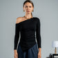 Woman wearing a black one-shoulder top and blue pants against a gray background