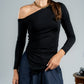 Woman wearing a black one-shoulder top and blue pants against a gray background
