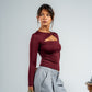 Woman wearing a burgundy long-sleeve top with cut-out design on a gray background