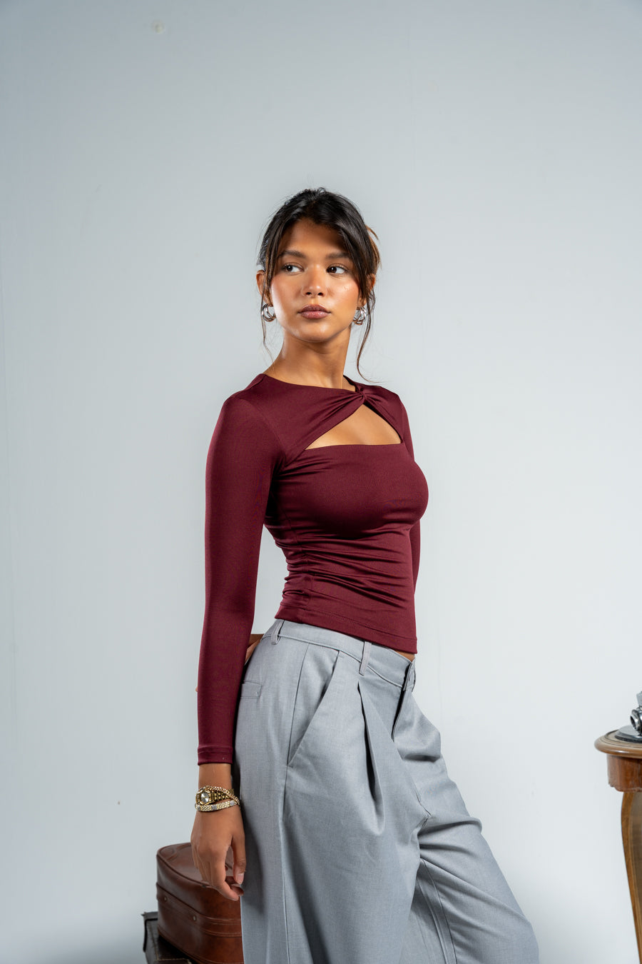 Woman wearing a burgundy long-sleeve top with cut-out design on a gray background
