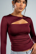 Woman wearing a burgundy long-sleeve top with cut-out design on a gray background