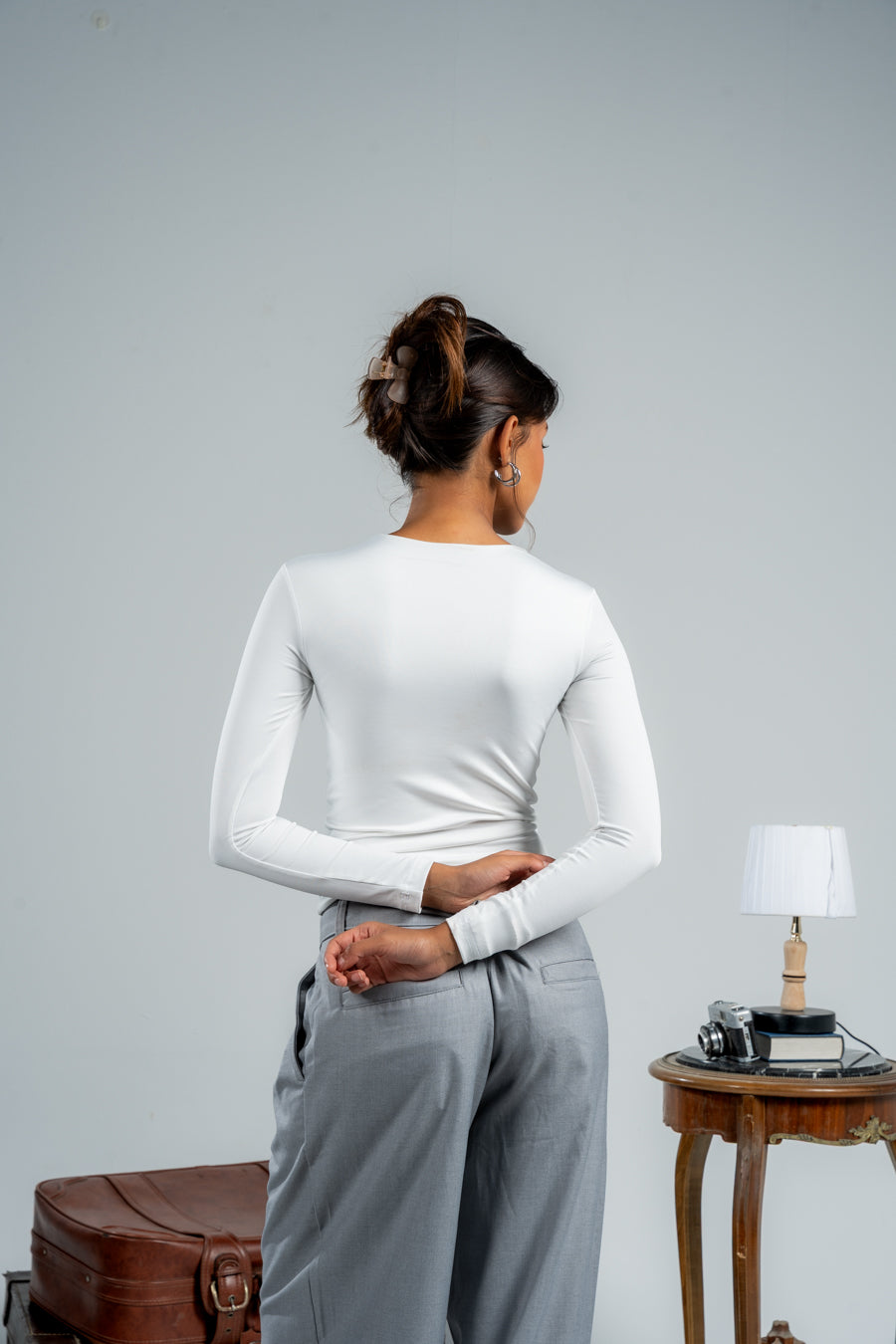 Person wearing a white long-sleeve top and gray pants against a plain background