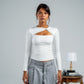 Woman wearing a white long-sleeve top with a cutout design and gray pants against a plain background.