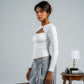 Woman in a white top and gray pants standing next to a suitcase against a plain background