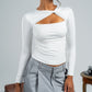 Woman wearing a white long-sleeve top with cut-out design and gray pants against a plain background