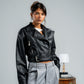 Person wearing a black leather jacket and gray pants against a plain background