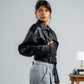 Woman wearing a black leather jacket and gray pants against a plain background