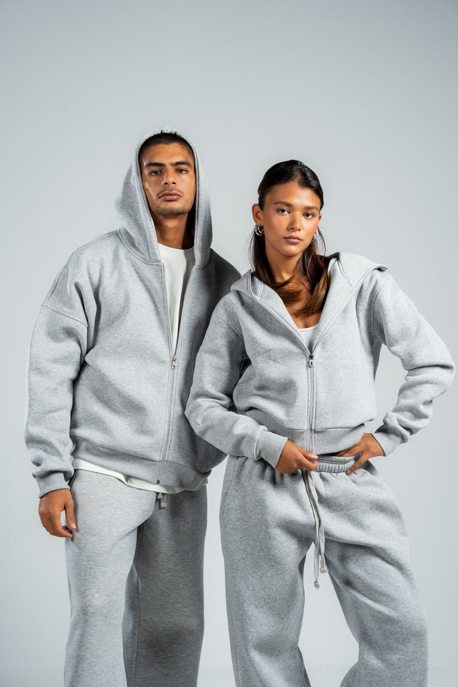 Two people wearing matching gray hoodies and pants on a plain background