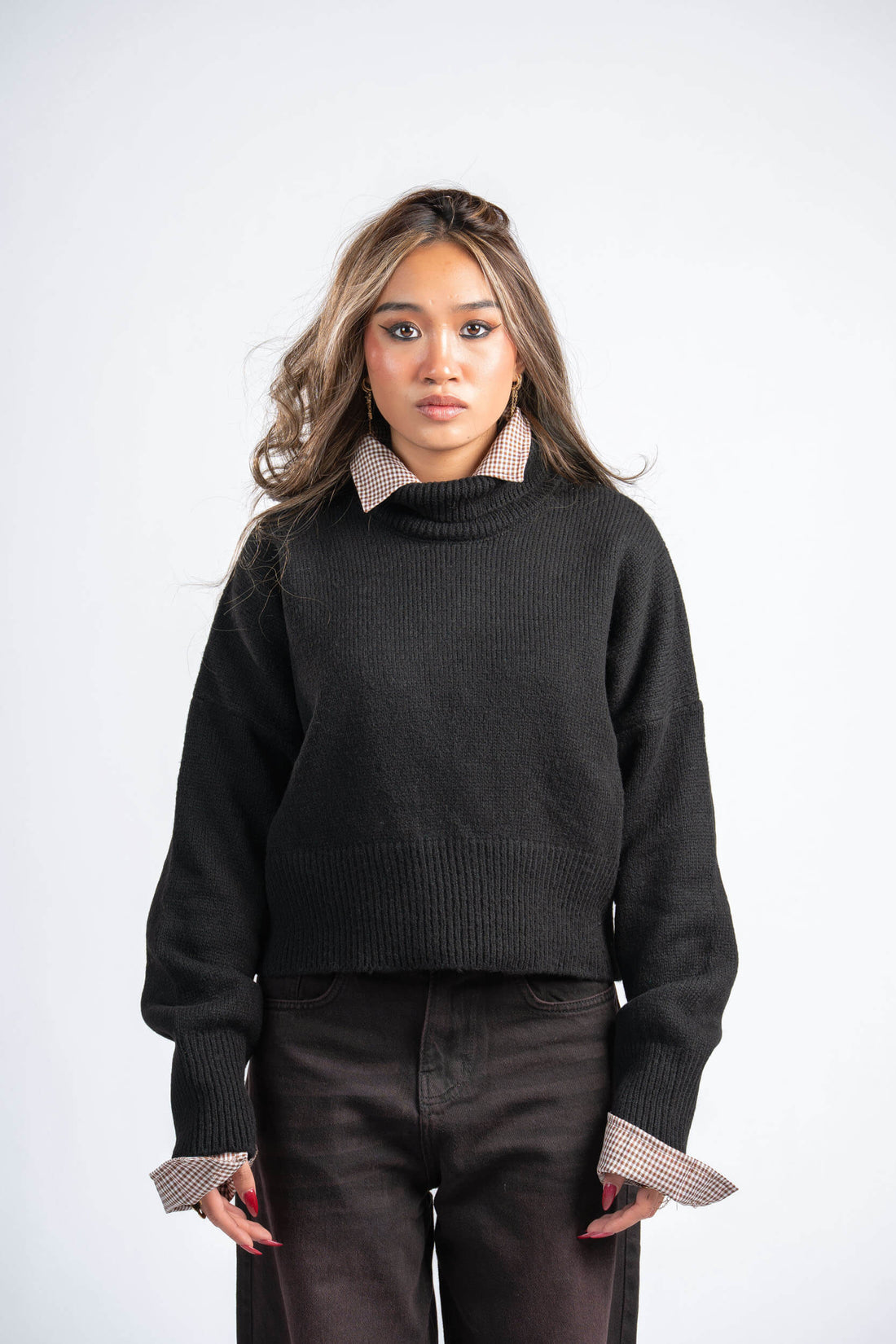 Woman wearing a black sweater with checkered cuffs and collar against a white background