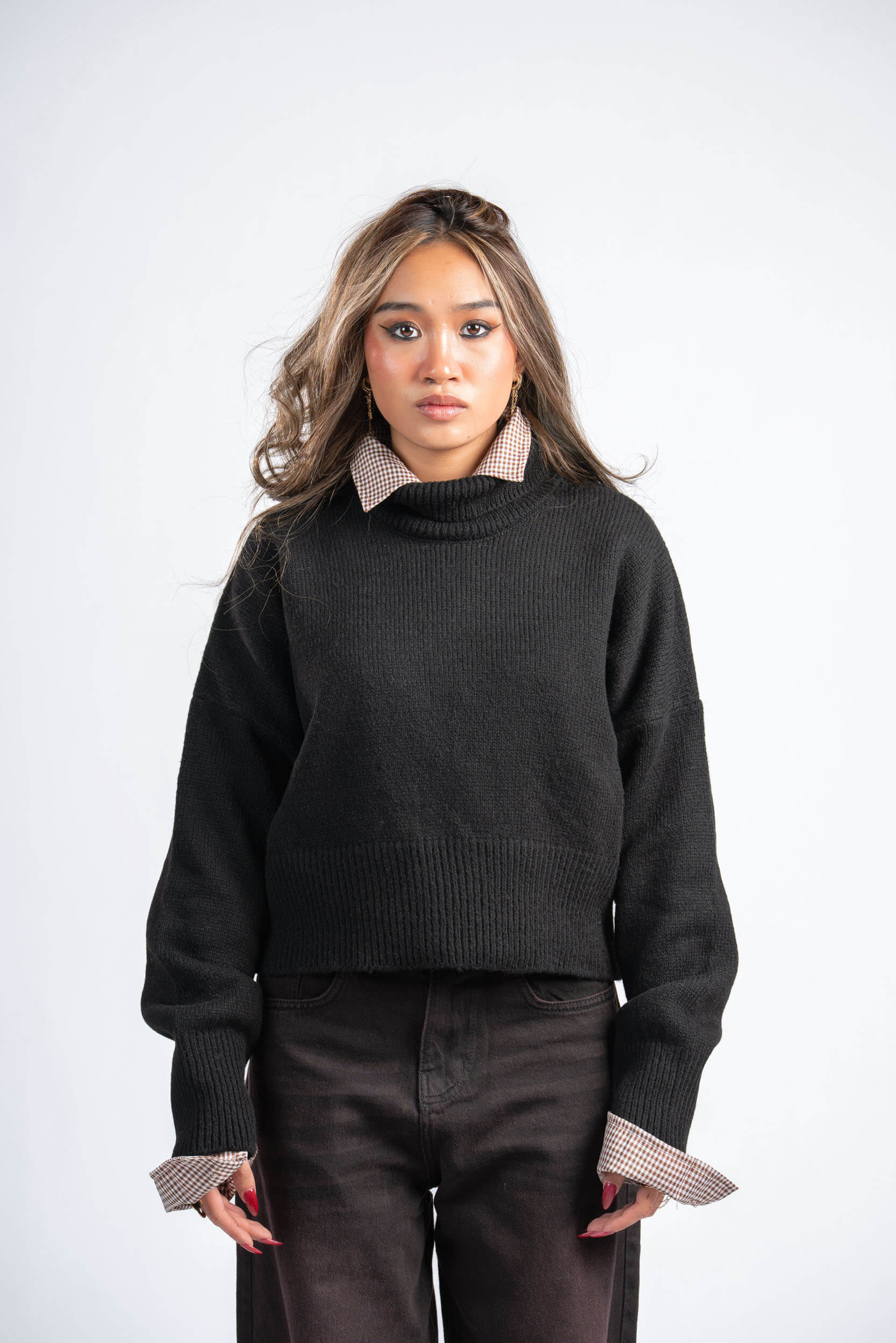 Woman wearing a black sweater with patterned cuffs and collar against a white background