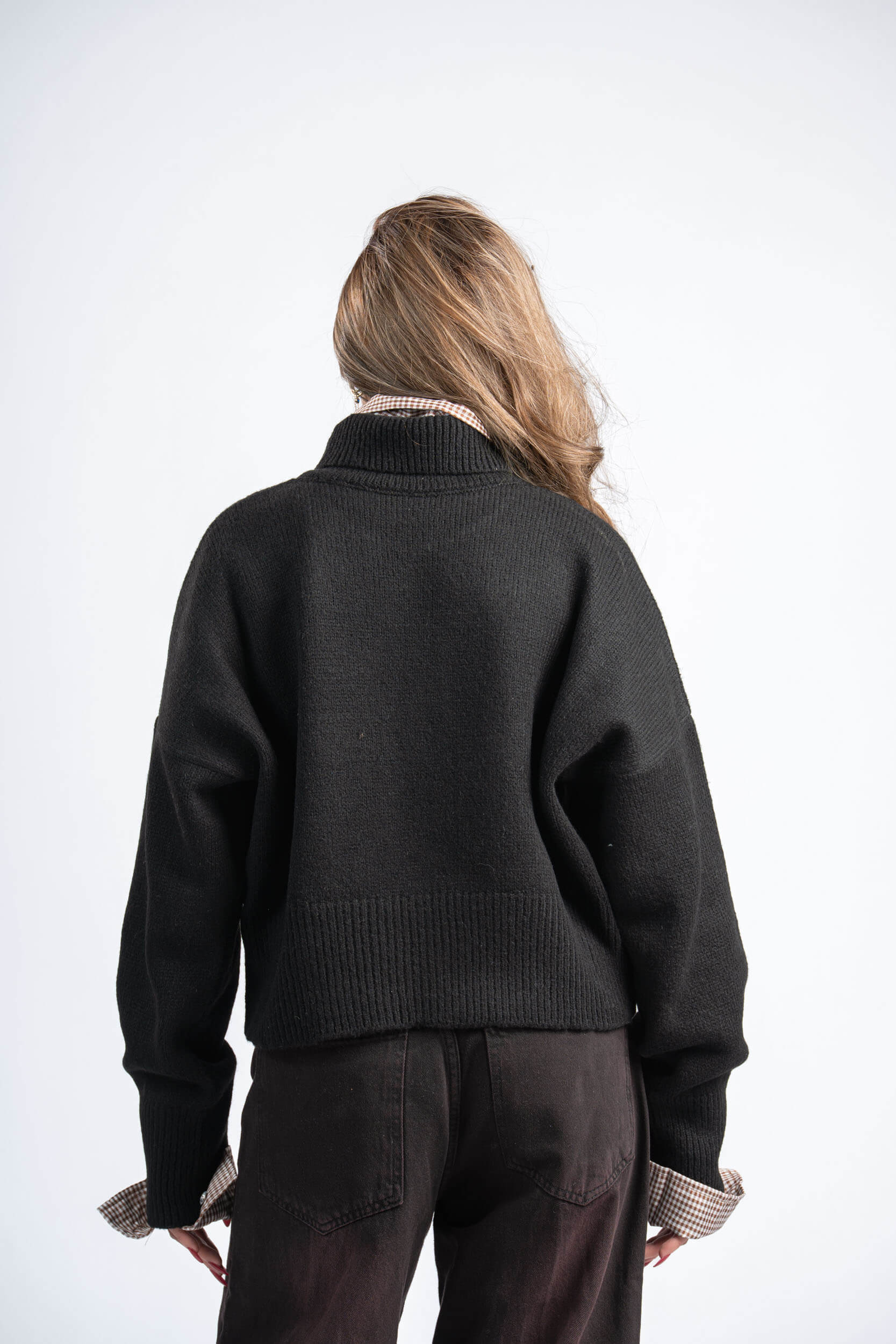 Person wearing a dark green sweater and brown pants on a white background