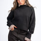 Woman wearing a black sweater with checkered cuffs and collar against a white background