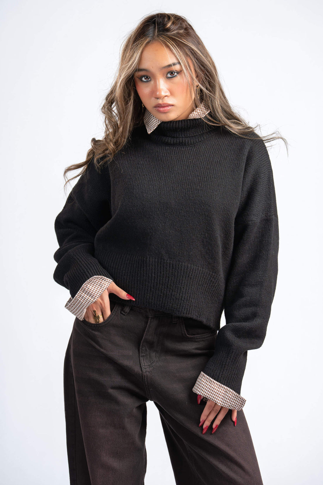 Woman wearing a black sweater with checkered cuffs and collar against a white background