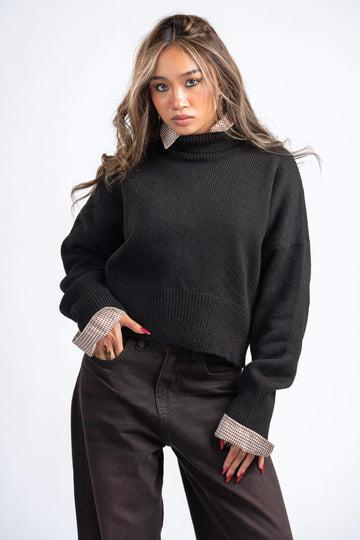 Woman wearing a black sweater with checkered cuffs and collar against a white background