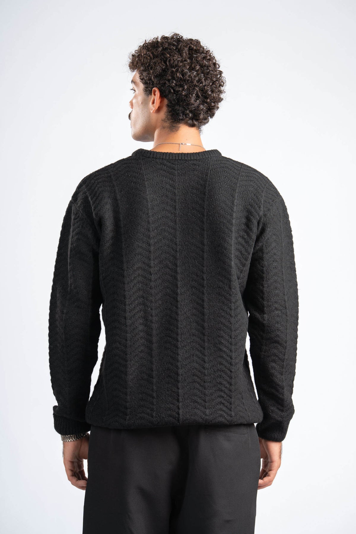 Person wearing a black sweater with a textured pattern on a white background