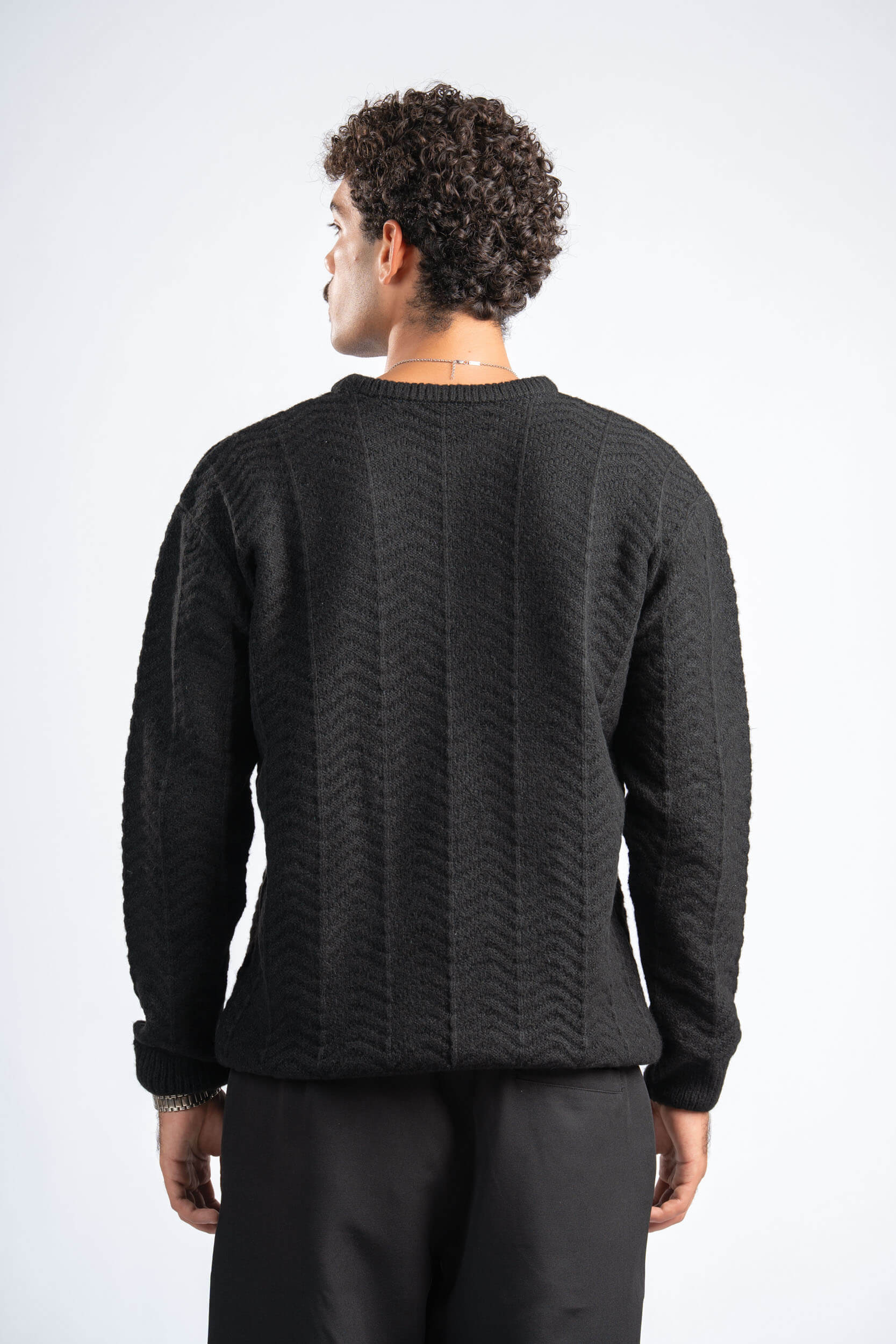 Person wearing a black sweater with a textured pattern on a white background