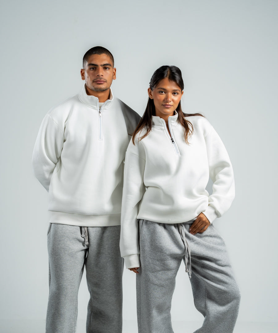 Two people wearing matching white hoodies and gray sweatpants on a plain background