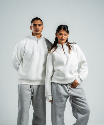 Two people wearing matching white hoodies and gray sweatpants on a plain background
