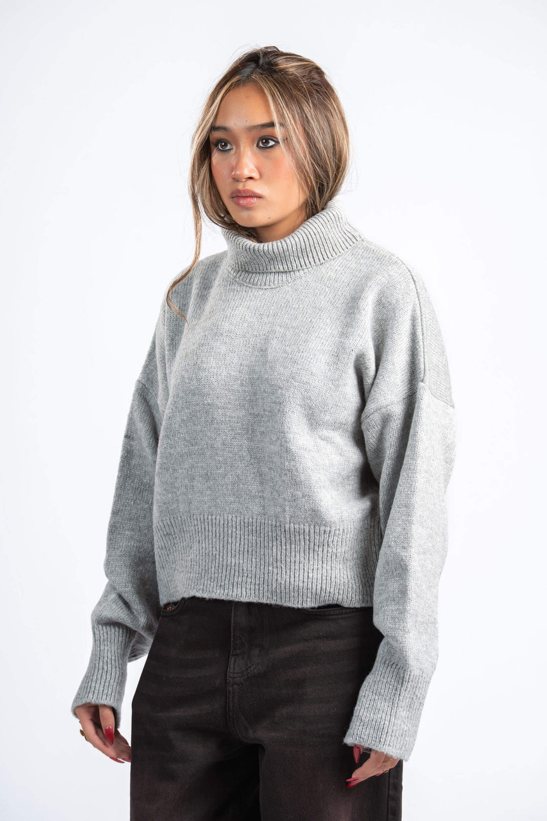 Person wearing a gray sweater and dark pants on a white background
