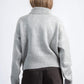 Person wearing a gray sweater and dark pants on a white background