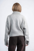 Person wearing a gray sweater and dark pants on a white background