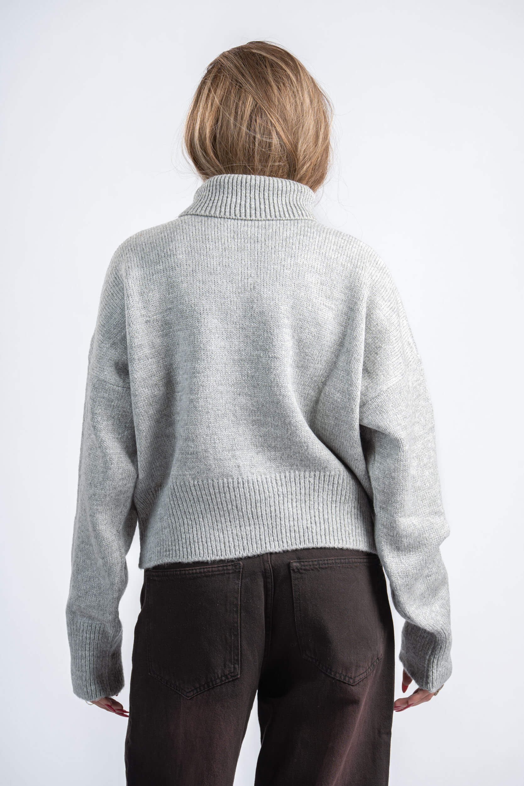 Person wearing a gray sweater and dark pants on a white background
