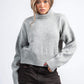 Person wearing a gray sweater and dark pants on a white background