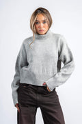 Person wearing a gray sweater and dark pants on a white background