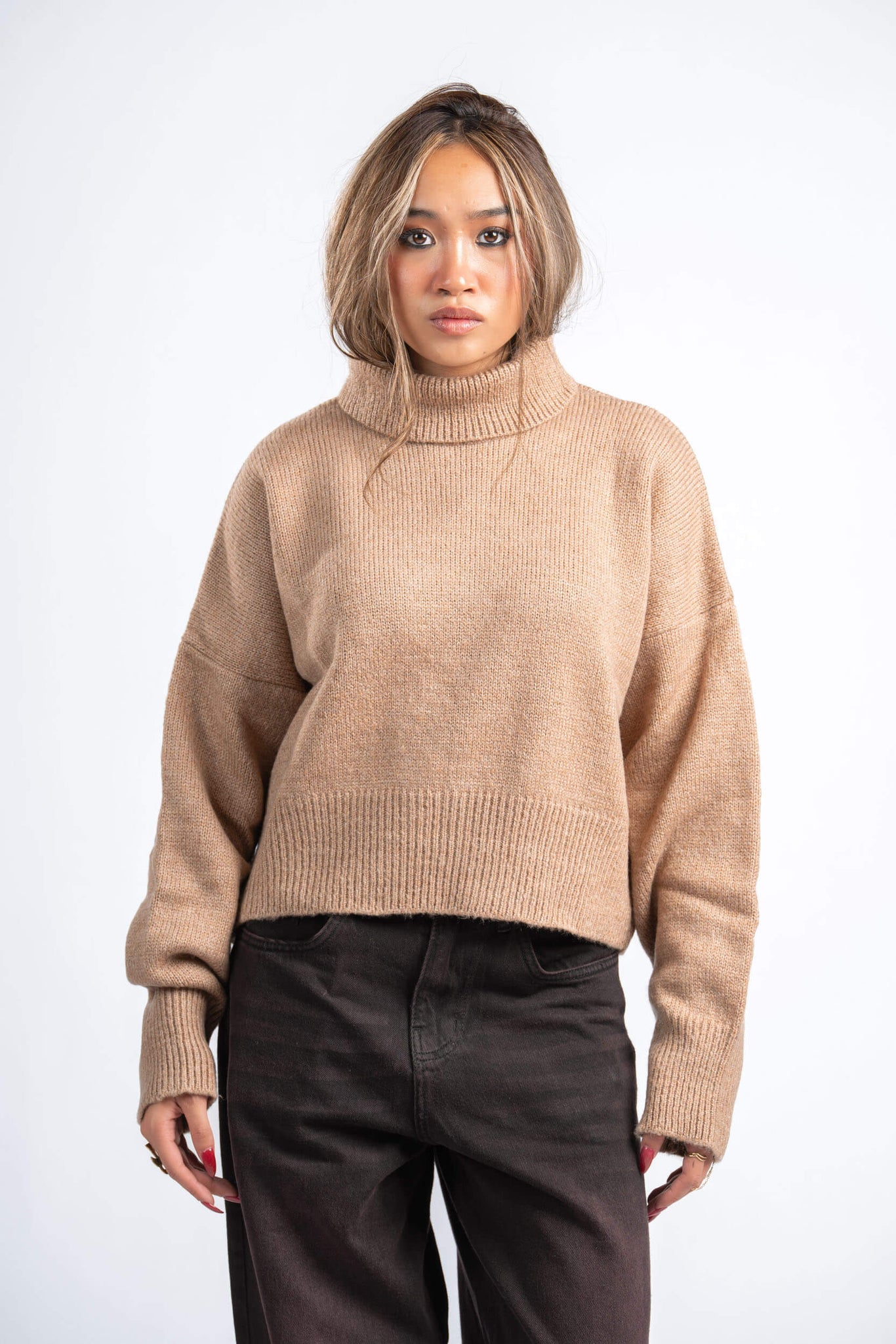 Woman wearing a beige sweater and dark pants on a white background