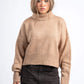 Woman wearing a beige sweater and dark pants on a white background