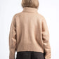 Person wearing a beige sweater and dark pants on a white background