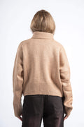 Person wearing a beige sweater and dark pants on a white background