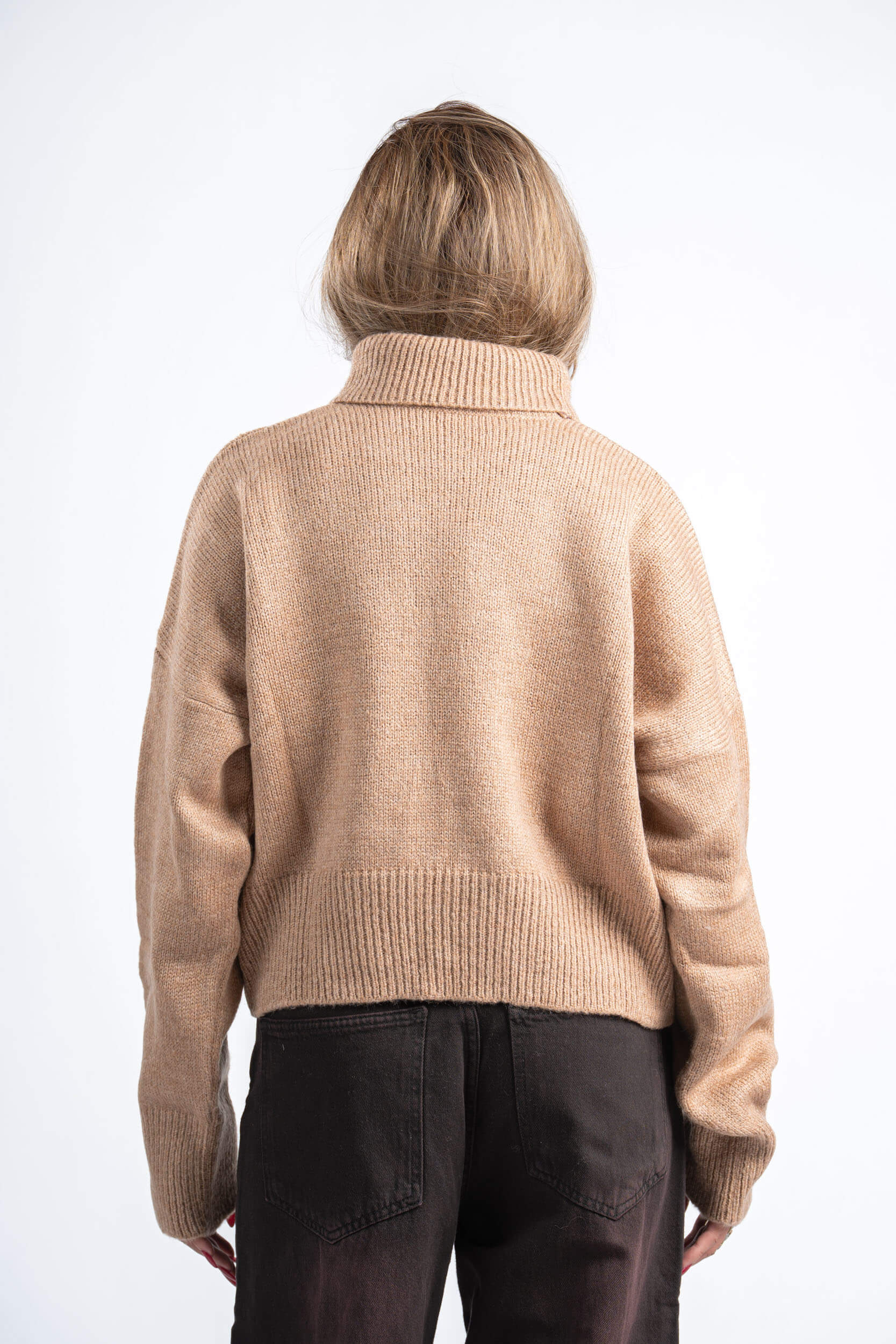 Person wearing a beige sweater and dark pants on a white background