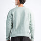 Man wearing a light green sweater and dark pants on a white background