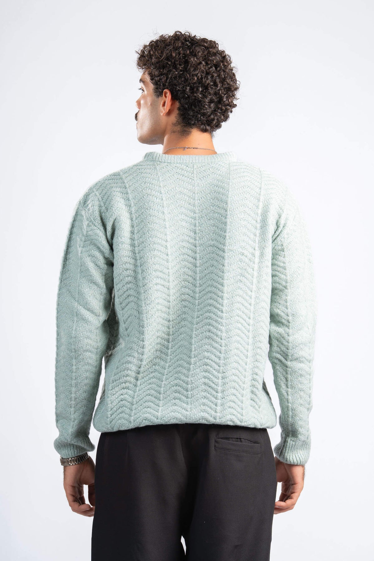 Man wearing a light green sweater and dark pants on a white background